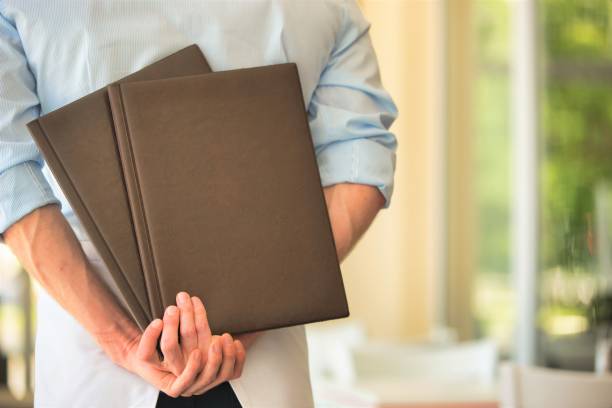 istock Rear view of young waiter holding menus while standing at restaurant 1191599477