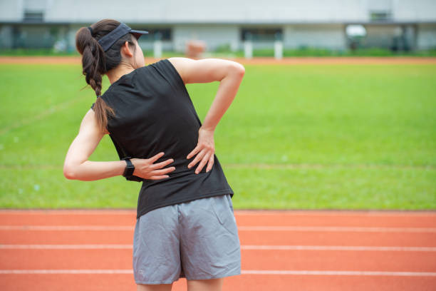 rückblick auf junge läuferin, die nach dem lauf auf der laufstrecke im stadion an rückenschmerzen oder sore taille leidet. - hüfte stock-fotos und bilder