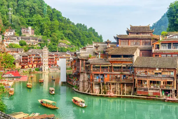 Gorgeous view of traditional wooden tourist boats on the Tuojiang River (Tuo Jiang River) in Phoenix Ancient Town (Fenghuang County), China. The Wanming Pagoda is visible in background.