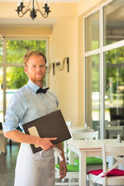 istock Portrait of confident young waiter holding menu while standing at restaurant 1191602329