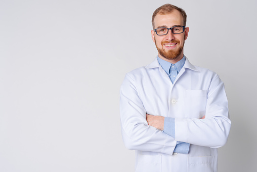 Retrato de joven feliz hombre barbudo médico usando anteojos con los brazos cruzados photo