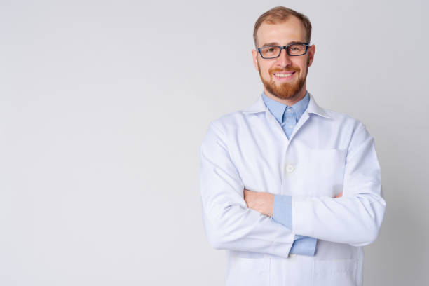 retrato de joven feliz hombre barbudo médico usando anteojos con los brazos cruzados - bata de laboratorio fotografías e imágenes de stock