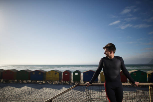 średnio dorosły surfer z pianką na plaży z widokiem na boki z kolorowymi chatami plażowymi - surf scene zdjęcia i obrazy z banku zdjęć