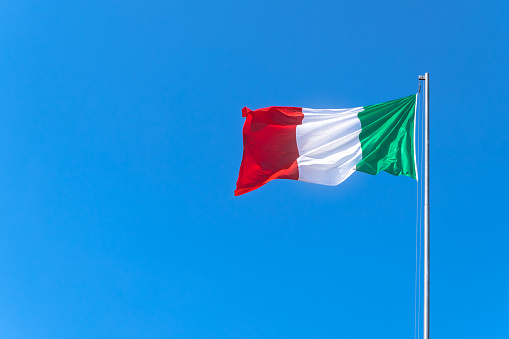 Italy flag waving against a blue sky background. Tricolor flag.