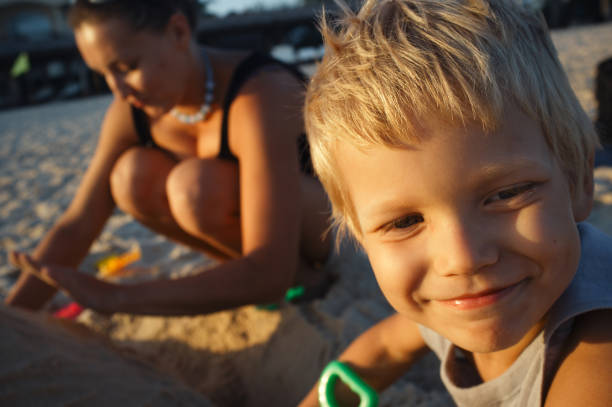 Building a sand castle Portrait of blond boy on the beach, on backstage his mom help him building a sand castle. olivia mum stock pictures, royalty-free photos & images