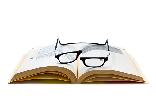 Black, prescription reading eye glasses with front connect magnetic bridge on an open book. Isolated on white background. High angle view.