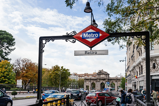 Madrid, Spain - November 2, 2019: Metro sign in Retiro Subway Station in Alcala Street against Puerta de Alcala with busy car traffic in the street