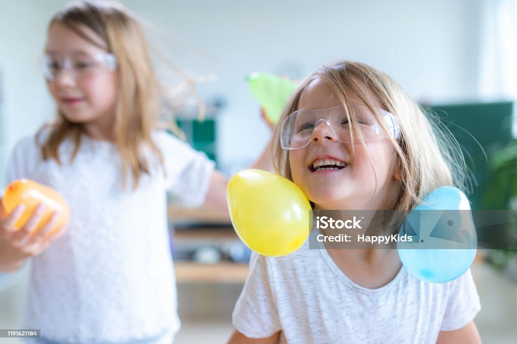 Students doing balloon experiment Cheerful girl creating static electricity in hair with balloon in laboratory. Static Electricity Stock Photo