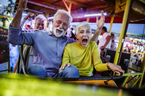 遊園地でジェットコースターを楽しむのんきなシニアカップル。 - rollercoaster carnival amusement park ride screaming ストックフォトと画像