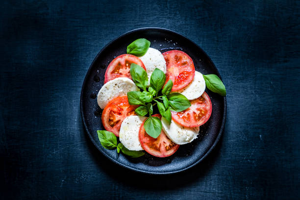 Caprese salad Top view of a caprese salad on a black plate. The salad is at the center of the image and is on a dark blackboard backdrop.  Low key DSLR photo taken with Canon EOS 6D Mark II and Canon EF 24-105 mm f/4L caprese salad stock pictures, royalty-free photos & images