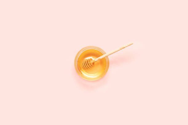 fresh honey in glass bowl with wooden spoon on pink background, top view - nobody maple tree deciduous tree tree imagens e fotografias de stock