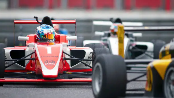 Man driving red Formula racing car on track.