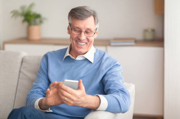 istock Positive Senior Gentleman Using Phone Sitting On Couch At Home 1191634890