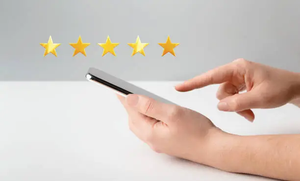 Photo of Woman hand using cellphone and rating with five stars