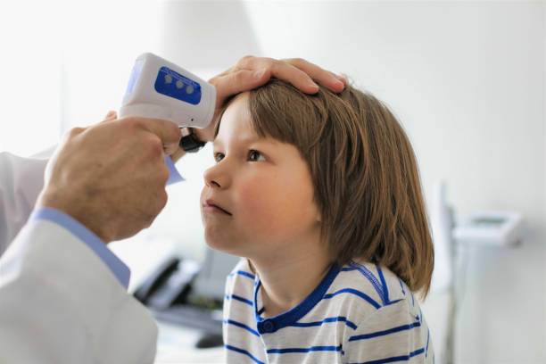 Cropped image of doctor measuring temperature of boy with infrared thermometer at hospital stock photo
