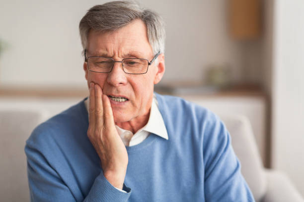 älterer mann mit zahnschmerzen sitzen auf sofa zu hause - zahnschmerz stock-fotos und bilder