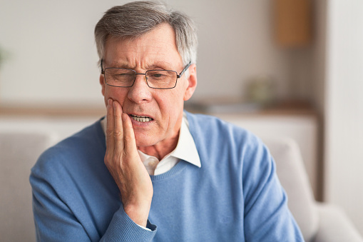 Hombre anciano que tiene dolor de dientes sentado en el sofá en casa photo
