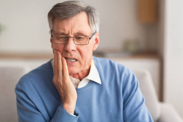 homem idoso que tem o toothache que senta-se no sofá em casa - dor de dente - fotografias e filmes do acervo