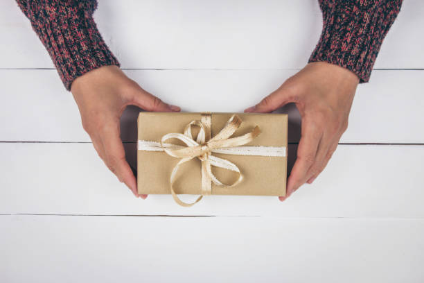 istock Woman's hands holding a gift with a golden bow on white wood background. 1191638338