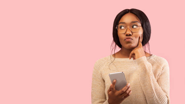 istock Black Woman Holding Mobile Phone Thinking Standing In Studio, Panorama 1191643749