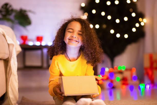 istock Happy african kid opening Xmas gift near decorated tree 1191644021