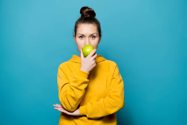 istock calm girl in a sweatshirt sniffs a fresh green apple 1191644268
