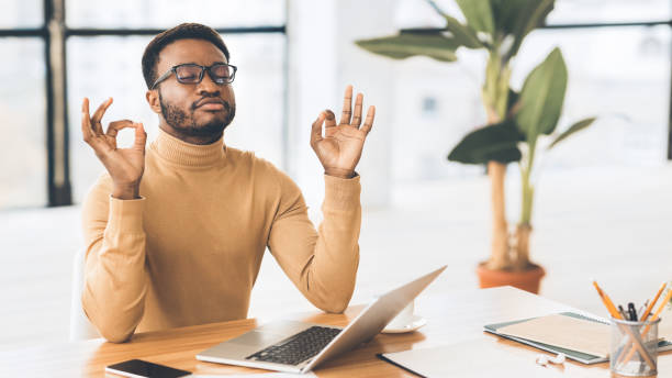 Calm black guy meditating while doing homework Stress Management. African student meditating, working on laptop, missing deadline. Panorama, free space managing stress stock pictures, royalty-free photos & images