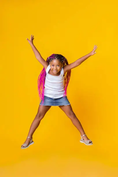 Photo of Cute little afro girl jumping over yellow studio background