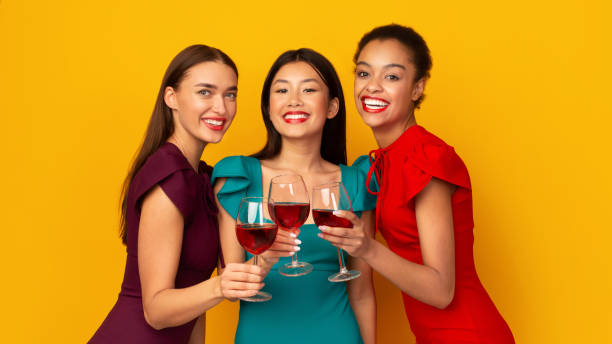 three girls with red wine clinking glasses, yellow background, panorama - asian ethnicity fashion model beautiful luxury imagens e fotografias de stock