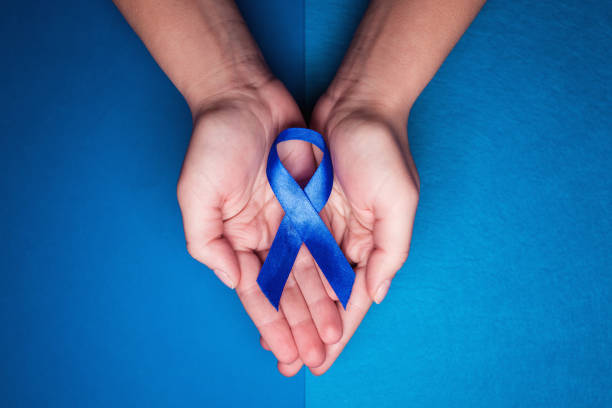 blue ribbon in support of trafficking and sexual slavery. Blue ribbon on female hands on a blue background blue ribbon in support of trafficking and sexual slavery. Blue ribbon on female hands on a blue background colorectal cancer photos stock pictures, royalty-free photos & images