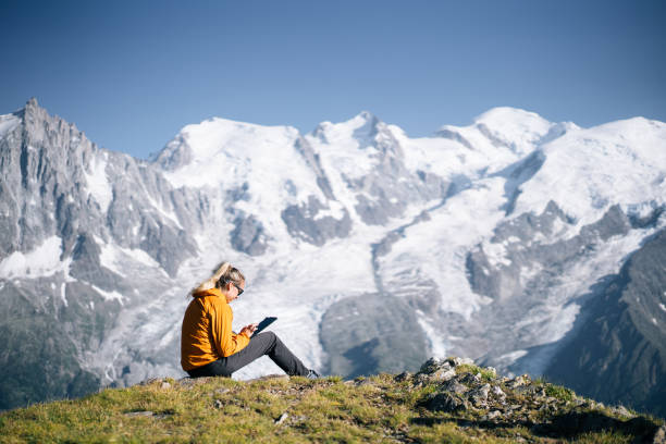 istock Female hiker sitting on mountain ridge uses digital tablet 1191652478