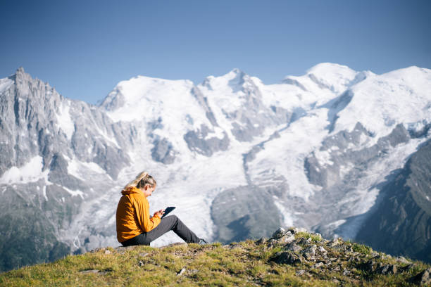 istock Female hiker sitting on mountain ridge uses digital tablet 1191653132