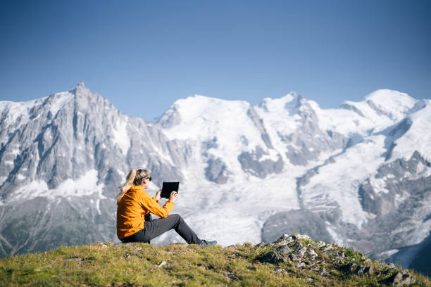 istock Female hiker sitting on mountain ridge uses digital tablet 1191653489