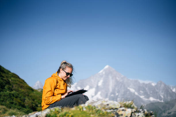 istock Female hiker sitting on mountain ridge uses digital tablet 1191653762