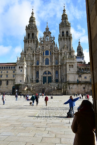 Santiago de Compostela, Spain. December 1, 2019. Pilgrims resting, having fun and taking pictures in front of the Cathedrals facade at Plaza del Obradoiro. View from Town Hall arch, Pazo de Raxoy (Palacio de Rajoy, Rajoys Palace).