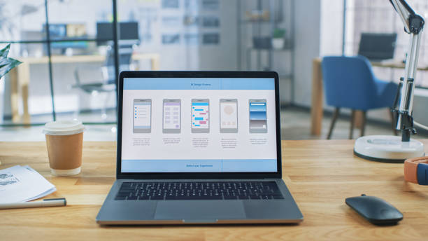istock Laptop on the Desk in the Office Shows Screen with Mobile Phone Application Design, Software UI Development. In the Background Creative Modern Open Space Office HUB with Professional Working 1191658284