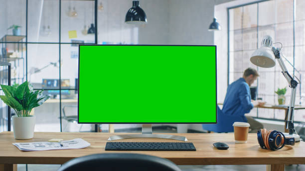 istock Wide Green Mock-up Screen Desktop Computer Standing on the Desk in the Modern Creative Office. In the Background High Ceiling Creative Loft for Developers and Designers where Professional Working at his Desk. 1191658338