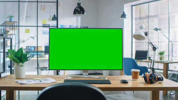 istock Wide Green Mock-up Screen Desktop Computer Standing on the Desk in the Modern Creative Office. In the Background Bright Creative Loft for Developers and Designers where Professional Working. 1191658353