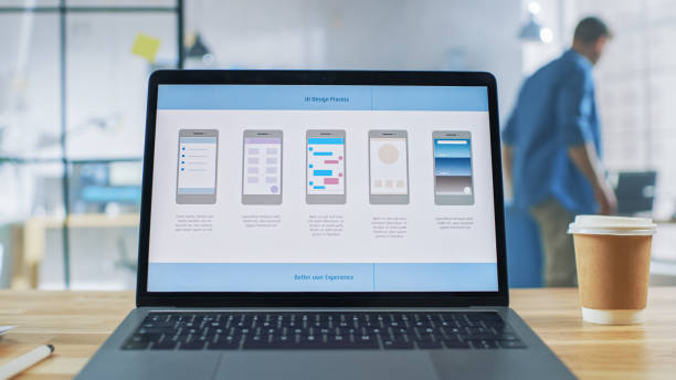 istock Laptop on the Desk in the Office Shows Screen with Mobile Phone Application Design, Software UI Development. In the Background Creative Modern Open Space Office HUB with Professional Working 1191658392