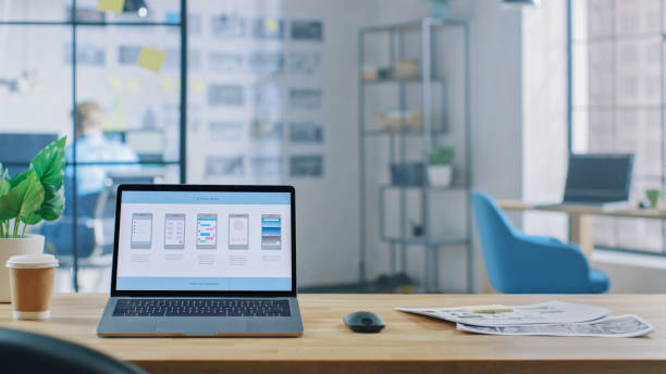 istock Laptop on the Desk in the Office Shows Screen with Mobile Phone Application Design, Software UI Development. In the Background Creative Modern Open Space Office HUB with Professional Working 1191658400