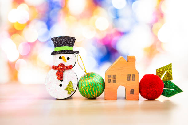 クリスマスコンセプトの背景、緑と赤のボールとぼやけたカラールボケの背景の上にミニチュア木製の家を持つ雪だるま - scarf hat green glove ストックフォトと画像