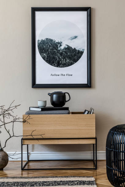 istock Modern scandinavian living room interior with black mock up poster frame, design commode, leaf in vase, black rattan basket, books and elegant accessories. Template. Stylish home decor. 1191664564