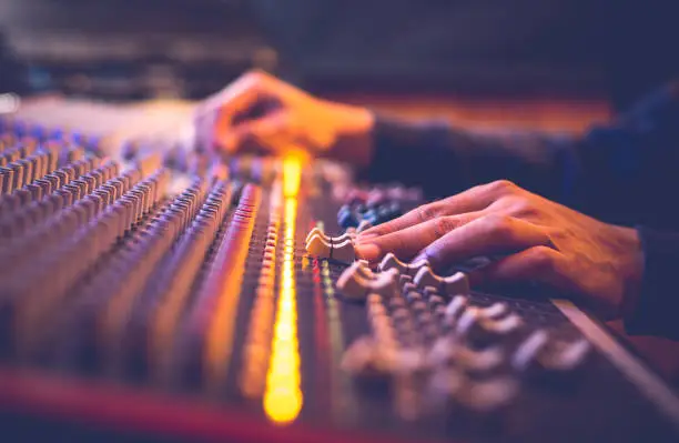 Photo of male producer, sound engineer hands working on audio mixing console in broadcasting, recording studio