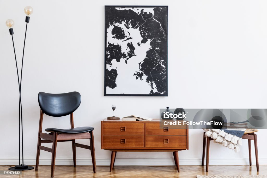 Interior design of living room with retro wooden commode, footrest, table lamp, rattan basket and elegant personal accessories. Minimalistic concept. Home decor. Mock up poster frame on the wall. Modern and stylish concept of wooden console commode and mock up frame. Home decor. Template Consoling Stock Photo