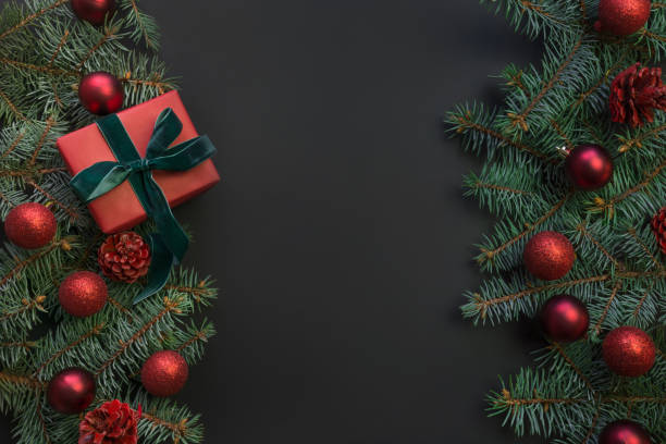 istock Christmas frame with gift box, evergreen branches, red balls on black. Space for text. 1191676885