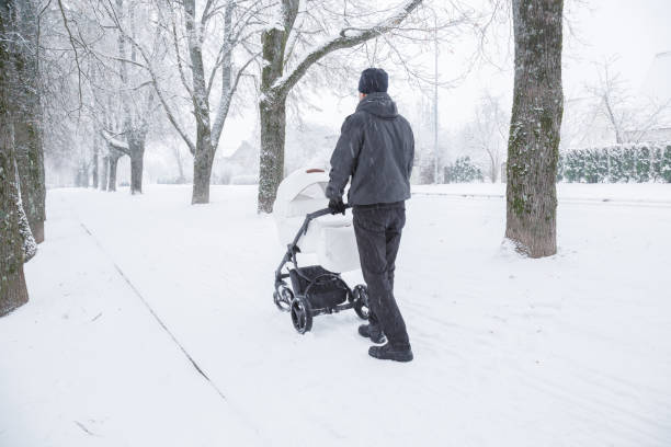 istock Young father pushing baby stroller. Man walking in blizzard. White overcast winter day. Back view. 1191677940