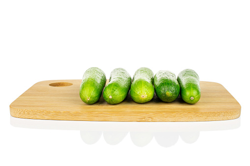 Group of five whole fresh green baby cucumber on bamboo cutting board isolated on white background