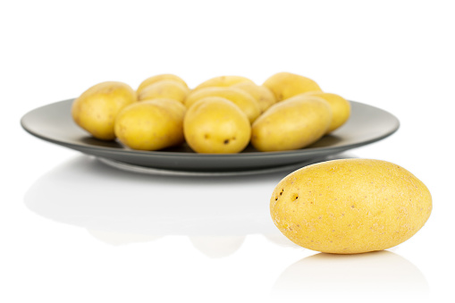 Lot of whole pale yellow potato on gray ceramic plate isolated on white background