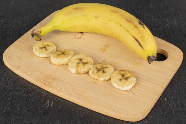 Group of one whole five slices of sweet yellow banana on bamboo cutting board on grey stone