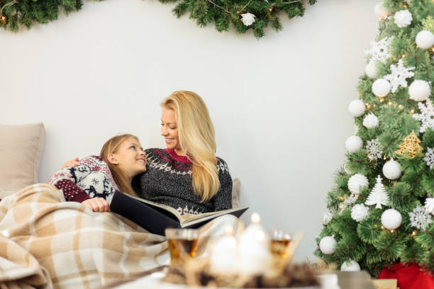 10代の少女は母親とソファに横たわり、居心地の良い毛布に包まれ、クリスマスの日に家族の写真アルバムで写真を見ます - 24403 ストックフォトと画像